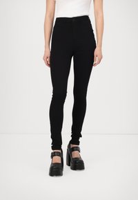 Zwarte high-waisted skinny jeans gemaakt van rekbaar materiaal, met een knoopsluiting, en gecombineerd met chunky zwarte platform schoenen.