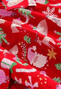 Röd tyg med julinspirerade tryck: jultomte, renar, snöflingor och juldekorationer i pastellfärger med en strukturerad mönster.