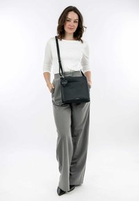 Black leather crossbody bag with a structured shape, featuring a heart-shaped charm and a smooth texture. Styled with gray wide-leg pants.
