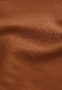 Tessuto marrone con una superficie morbida e tessurizzata. Il tessuto presenta un motivo di tessitura liscio ed uniforme, creando profondità e dimensione sottili.