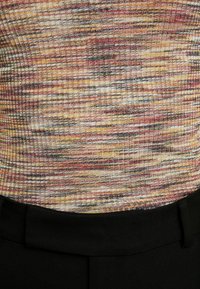 Haut côtelé multicolore avec des tons chauds de jaune, orange, rouge et noir, présentant une coupe ajustée et un tissu texturé, associé à une ceinture noire.