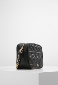 Borsa a tracolla nera in pelle trapuntata con dettagli in oro, dotata di chiusura con cerniera e tracolla a catena. Forma compatta e rettangolare con texture dettagliata.