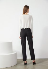 Suéter de punto blanco con corte holgado y mangas largas, combinado con pantalones negros de talle alto, que presentan una textura suave y un diseño ajustado.