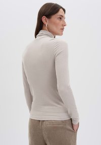 Slim-Fit, langärmliges Turtleneck-Top aus leicht beigem Rippstoff. Verfügt über einen hohen Kragen und eine weiche Textur, kombiniert mit Cordhosen.