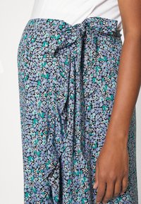 Květinová sukně ve světle modré, zelené a černé barvě, s malými květinovými vzory, volným střihem a zavazovací pasem pro nastavitelnou velikost.