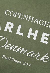 Oļīvzaļš kokvilnas T-krekls ar baltu drukātu tekstu: "Copenhagen", "Barlhet", "Denmark" un "Established 2017" dažādos fontu stilos.