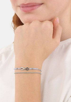 Bracciale argentato con simbolo dell'infinito, accompagnato da perline azzurro pallido e un design di catena delicato. Indossato su un polso.