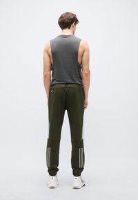 Roupa atlética com top cinza sem mangas e calças verde-oliva. As calças apresentam acentos verde claro e um design com três riscas próximo aos punhos.