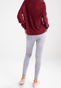 Maglione lavorato a maglia color bordeaux con vestibilità ampia e maniche a volant, abbinato a jeans skinny grigi chiari e scarpe slip-on rosa chiaro.