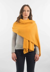 Sennepsgul sjal hængende over en grå sweater, der har et blødt, tekstureret stof med en let fald. Enkel, ingen synlige mønstre.