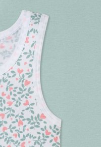 White tank top with a floral pattern featuring green leaves and small pink hearts, paired with a soft mint-green background.