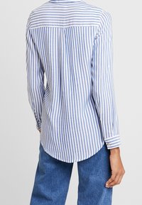 Chemise rayée bleu et blanc, manches longues, ourlet arrondi, poignets boutonnés, tissu doux, empiècement au dos avec un pli pour plus de liberté de mouvement.