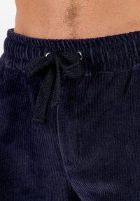 Granatowe spodnie dresowe z sztruksu z talią na ściągacz ozdobioną czarnymi akcentami i prążkowaną fakturą, wykazujące subtelny połysk tkaniny.