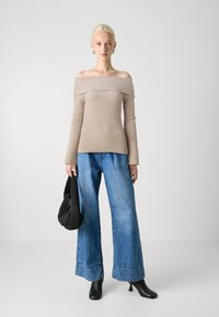 Haut beige à rayures, décolleté épaule, jean large bleu, bottes à talons noires, et un sac tissé noir. Silhouette simple et élégante.