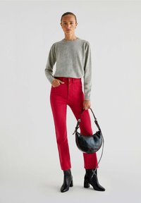 Grå langærmet sweater med puffede skuldre, parret med tætsiddende røde højtaljede jeans. Modellen holder en sort halvmåneformet håndtaske.