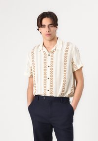 Korte mouw, knoopshirts in crème met een bruin geometrisch patroon. Gemaakt van lichtgewicht stof, met een gekleed decolleté en een relaxte pasvorm.