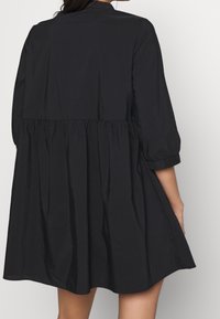 Abito nero con un design a strati svasato, maniche a tre quarti e una texture liscia. Presenta un colletto semplice e una cucitura in vita arricciata.