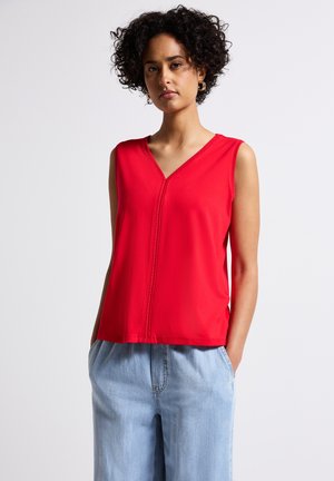 Haut sans manches rouge avec un col en V et un détail de couture centrale ; fabriqué en tissu lisse, coupe décontractée, associé à un pantalon ample bleu clair.