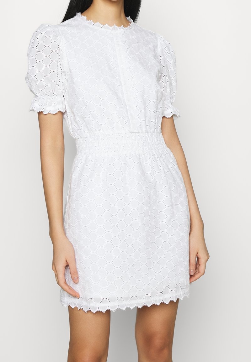 Bílé krátké šaty z broderie anglaise látky s nabíranými rukávy, elastickým pasem, vlnkovaným lemem a knoflíkovým detailem na krku.