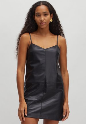 Robe en cuir noir avec des bretelles fines, décolleté en V, design ajusté et texture lisse. Présente un détail de couture à l'avant et arrive au milieu des cuisses.