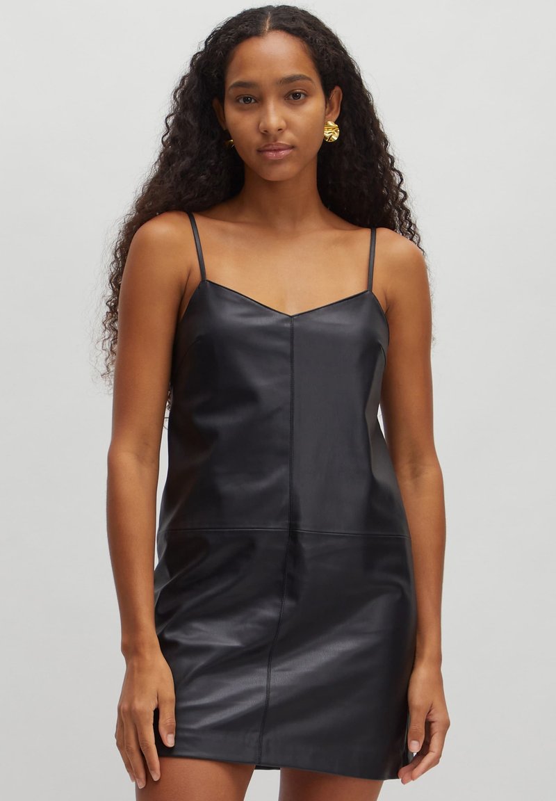 Robe en cuir noir avec des bretelles fines, décolleté en V, design ajusté et texture lisse. Présente un détail de couture à l'avant et arrive au milieu des cuisses.