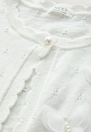 Cardigan alb din tricot, cu margine cu dantelă, un nasture din perlă și aplicații decorative cu fluturi. Textură moale cu detalii cu găuri.