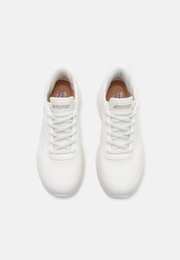 Chaussures de sport blanches avec une tige en maille et des accents texturés. Présentent des lacets plats, un col rembourré et un logo sur la languette. Semelle en caoutchouc flexible.