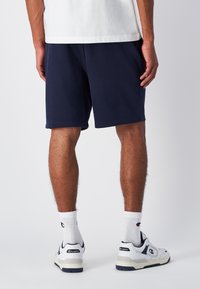 Marineblaue Shorts aus Baumwollmischgewebe mit entspannter Passform und kontrastierenden Nähten, kombiniert mit weißen Sportsocken und Schuhen.