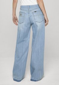 Svetlomodré džíny s širokými nohavicami a vertikálnymi pruhmi, bavlnený materiál, štandardné vrecká a vyblednutý efekt na lemovaní.
