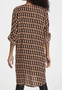 Long blouse in lightweight fabric, featuring a geometric pattern of brown, camel, and pink diagonal lines. Rolled sleeves and loose fit.
