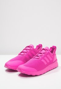 Bright pink athletic shoes with a mesh upper, lace-up closure, and three stripes on the side. Cushioning sole with textured detailing.