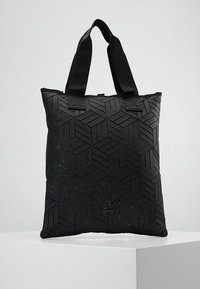 Sac fourre-tout noir avec un motif géométrique texturé, doté de courtes poignées en tissu et d'une fermeture éclair en haut. Fabriqué en matériau synthétique.