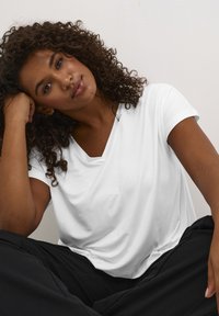 Vit v-ringad t-shirt med en mjuk, slät textur, korta ärmar och en lätt avslappnad passform, kombinerad med svarta byxor.