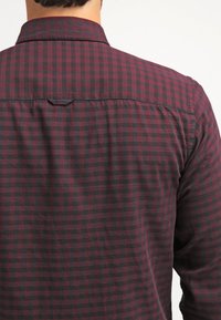 Camicia a quadri bordeaux e nera con colletto e dettagli in yoke. Tessuto morbido con vestibilità rilassata e orlo posteriore curvo.