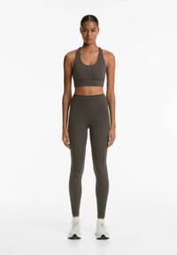 Sportbeha en hoge taille legging in een donkere olijfgroene kleur, gemaakt van een soepele, elastische stof met een naadloos ontwerp. Gepaard met witte sneakers.