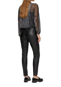 Zwarte, aansluitende faux leren broek gecombineerd met een sheer, sprankelend zwart top met pofmouwen en een cropped ontwerp. Glanzende zwarte schoenen.