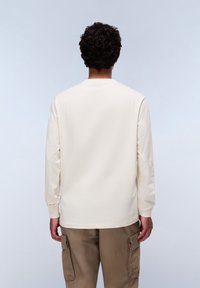 Langarm, rondhals T-shirt van zachte, crèmekleurige katoen, met ribgebreide manchetten. Gecombineerd met stevige, beige cargobroeken met zijzakken.