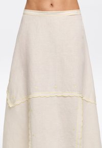 Linen skirt in light beige with yellow embroidered details and scalloped edges. A-line shape, knee-length, featuring textured fabric.