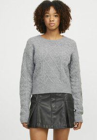Maglione grigio a maglia con motivo a trecce, colonna rotonda e maniche lunghe, abbinato a una gonna nera in ecopelle.