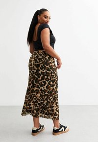 Haut noir ajusté avec découpe dans le dos et longue jupe léopard dans des tons beige et marron, associée à des baskets noires et crème.