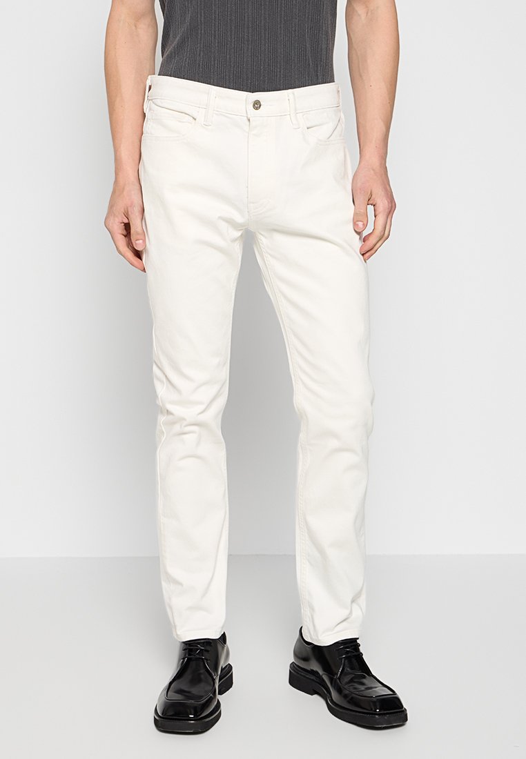 Witte katoenen jeans met een slim fit, met contrasterende stiksels, voorzakken en een enkele knoopsluiting. Draagt met glanzende zwarte schoenen.