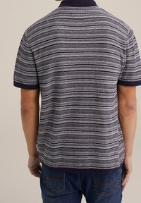 Polo à manches courtes avec un col bleu marine, présentant un motif rayé dans des nuances de gris et de blanc. Le tissu a une finition texturée.