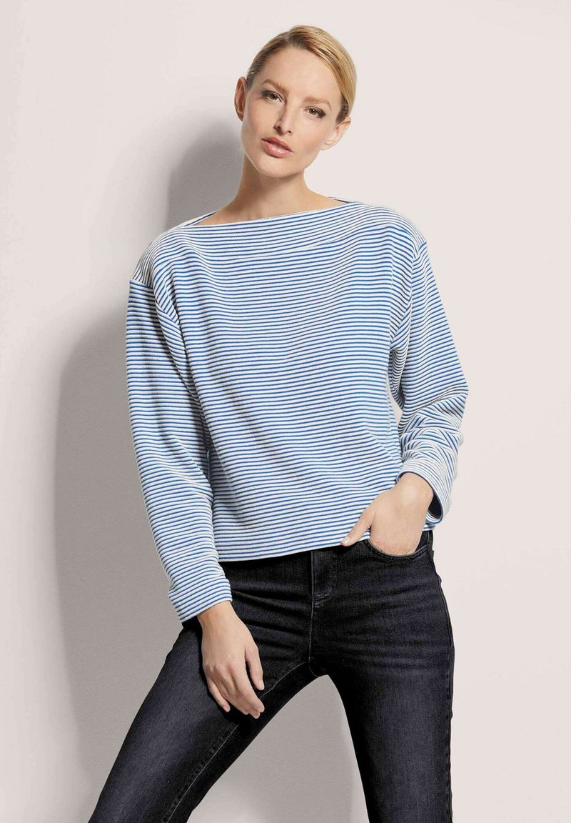 Gestreiftes Langarmoberteil in Hellblau und Weiß, mit weitem Bootsausschnitt und lässiger Passform. Kombiniert mit dunklen Jeans.