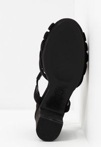 Sandale à talon haut en daim noir avec une semelle noire texturée et un talon minimaliste. Dotée de brides croisées pour un maintien sécurisé.