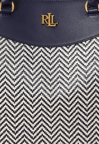 Granatowa torebka z plecionym wzorem chevron w białym kolorze. Wyposażona w złote akcesoria i gładki skórzany pasek na górze.