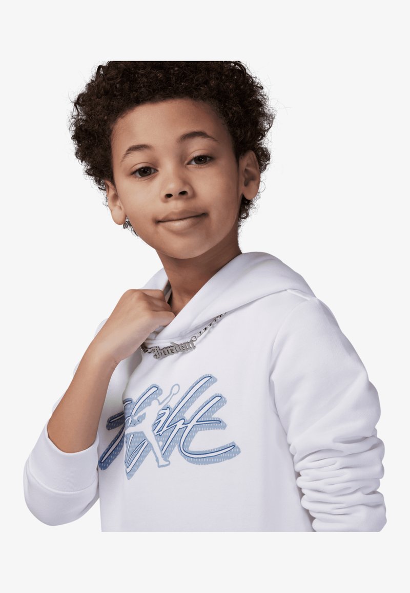 Sudadera blanca con estampado gráfico azul "Style", capucha con cordones y puños acanalados. Presenta un collar de cadena plateada. Modelo joven.