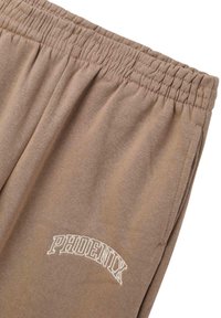 Pantaloni da jogging color taupe con vita elastica e ricamo bianco "PHOENIX" sul lato sinistro, realizzati in un morbido tessuto testurizzato.