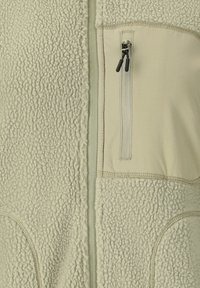 Lichtbeige fleecejack met een centrale ritssluiting en een verticale borstzak met ritssluiting met zwarte ritstrekker.