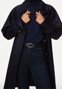 Abrigo de marina con un ajuste holgado, gran cuello y detalles de botones, llevado sobre un cuello de tortuga azul marino y jeans oscuros, con una hebilla de cinturón ovalada de plata.