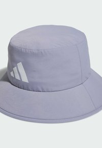 Lawendowy kapelusz typu bucket wykonany z lekkiego materiału, z płaską koroną i szerokim rondem. Na boku znajduje się białe logo. Gładka faktura.